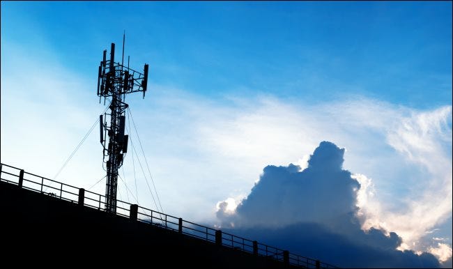 A 5G cellular tower against a blue sky with white clouds. 