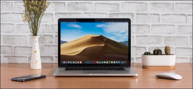 An open MacBook sitting on a desk next to a mouse and smartphone.