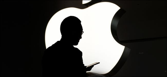 A silhouette of a person using an iPhone in front of an Apple logo.