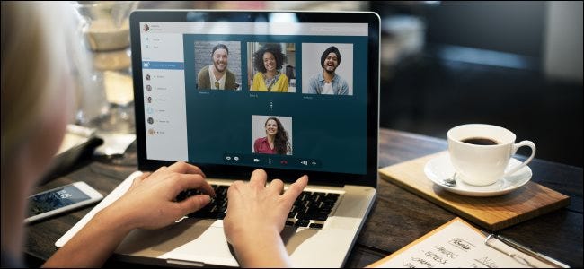 A woman's hands on the keyboard of her laptop, with four people in a video-conference call on the screen. 